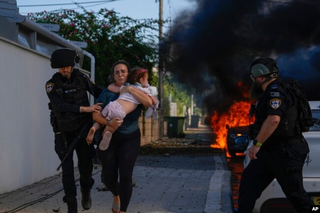 Cảnh sát di tản một người phụ nữ và một đứa trẻ khỏi địa điểm bị trúng tên lửa bắn từ Dải Gaza, ở Ashkelon, miền nam Israel, ngày 7 tháng 10 năm 2023.