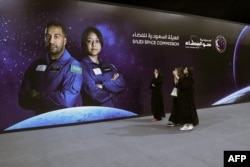 FILE - People walk past a poster with the picture of Saudi Space Commission astronauts Ali Al-Qarni, left, and Rayyanah Barnawi, of the Axiom Mission 2, at a government-organized viewing party in Riyadh, May 21, 2023.