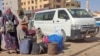 People wait with their luggage at a bus stop in southern Khartoum, May 8, 2023, as fighting continues between Sudan's army and paramilitary forces.