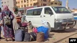 People wait with their luggage at a bus stop in southern Khartoum, May 8, 2023, as fighting continues between Sudan's army and paramilitary forces.