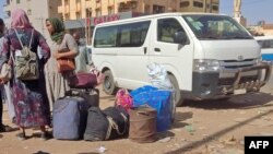 People wait with their luggage at a bus stop in southern Khartoum, May 8, 2023, as fighting continues between Sudan's army and paramilitary forces.