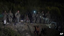 Texas National Guard members stand along a stretch of razor wire as migrants try to cross into the United States on the banks of the Rio Grande, as seen from Matamoros, Mexico, May 11, 2023.