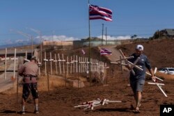 Ethan Meyers, a la derecha, lleva cruces para honrar a las víctimas muertas en un reciente incendio forestal en Lahaina, Hawaii, el martes 22 de agosto de 2023.