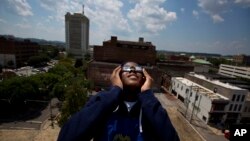 FILE - Justin Coleman, of Birmingham, Ala., holds his glasses up to his eyes as he watches the solar eclipse atop a parking structure, Aug. 21, 2017, in Birmingham.