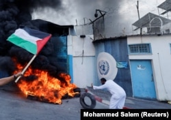 Seorang pria Palestina membakar ban di luar markas UNRWA yang menuntut UNRWA untuk membangun kembali rumah mereka yang hancur selama pertempuran Israel-Gaza pada 2014, di Kota Gaza, 19 September 2022. (Foto: REUTERS/Mohammed Salem)