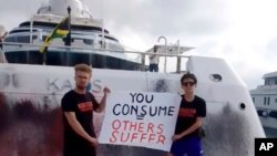In this screengrab from video provided by Karen Killeen, activists hold a sign in front of a super yacht belonging to Walmart heiress Nancy Walton Laurie, after spray-painting it in Ibiza, Spain, July 16, 2023.