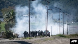 French gendarmes stand amid tear gas smoke as clashes occur with pro-independence protesters during the removal of a roadblock on Paul-Emile Victor avenue in Dumbea on the French Pacific territory of New Caledonia, June 24, 2024. 