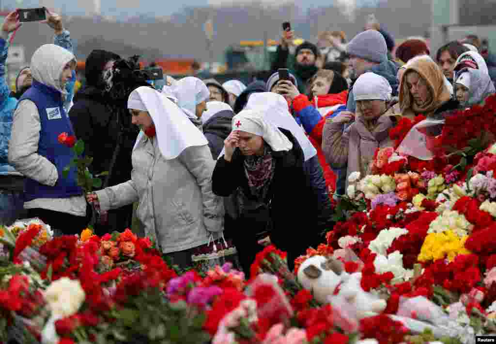 Orang-orang meletakkan bunga dan berdoa di tempat peringatan darurat bagi para korban serangan penembakan yang diadakan di luar tempat konser Balai Kota Crocus di pinggiran Moskow, Rusia. (Reuters)&nbsp;