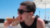 FILE - Alex Krisulas of Staten Island, New York, eats a slice of pizza on the boardwalk in Asbury Park, New Jersey, May 21, 2021. 