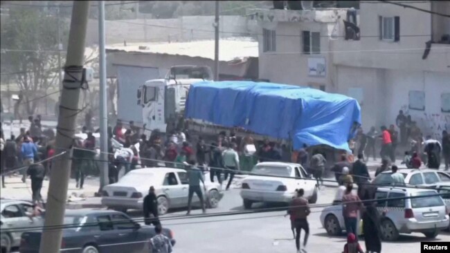 Orang-orang mengejar di belakang konvoi truk bantuan yang melaju ke Gaza dari penyeberangan Rafah, 9 April 2024, dalam tangkapan layar yang diambil dari video. (REUTERS TV/via REUTERS)