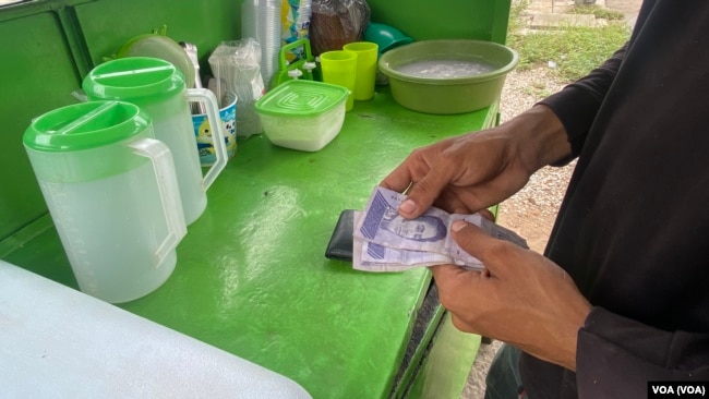Andry Araque, vendedor de cocos en Maracaibo, repasa sus ganancias en bolívares y dólares la mañana de este miércoles. Como el resto de los comerciantes informales, fija sus precios según la fluctuación del dólar estadounidense.