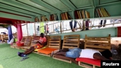 FILE - A man reads a book while other one takes a nap, at a makeshift 'library' under a bridge, at the Luanda surburbs in Angola, August 22, 2022.