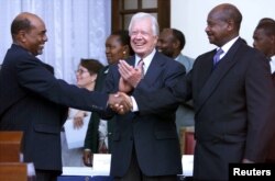 រូបឯកសារ៖ ប្រធានាធិបតីស៊ូដង់លោក Omar al-Bashir (ឆ្វេង) និង​ប្រធានាធិបតី​អ៊ូហ្គង់ដា​លោក Yoweri Museveni (ស្តាំ) ចាប់រលាក់ដៃគ្នា​នៅ​ថ្ងៃ​ទី៨ ខែធ្នូ ១៩៩៩ បន្ទាប់ពី​បានចុះហត្ថលេខា​លើ​កិច្ចព្រមព្រៀង​មួយ​ដែល​មាន​គោលបំណង​កែលម្អ​ទំនាក់ទំនង ខណៈ​ដែល​អតីត​ប្រធានាធិបតី​អាមេរិក​លោក Jimmy Carter (កណ្តាល) សម្លឹង​មើល។