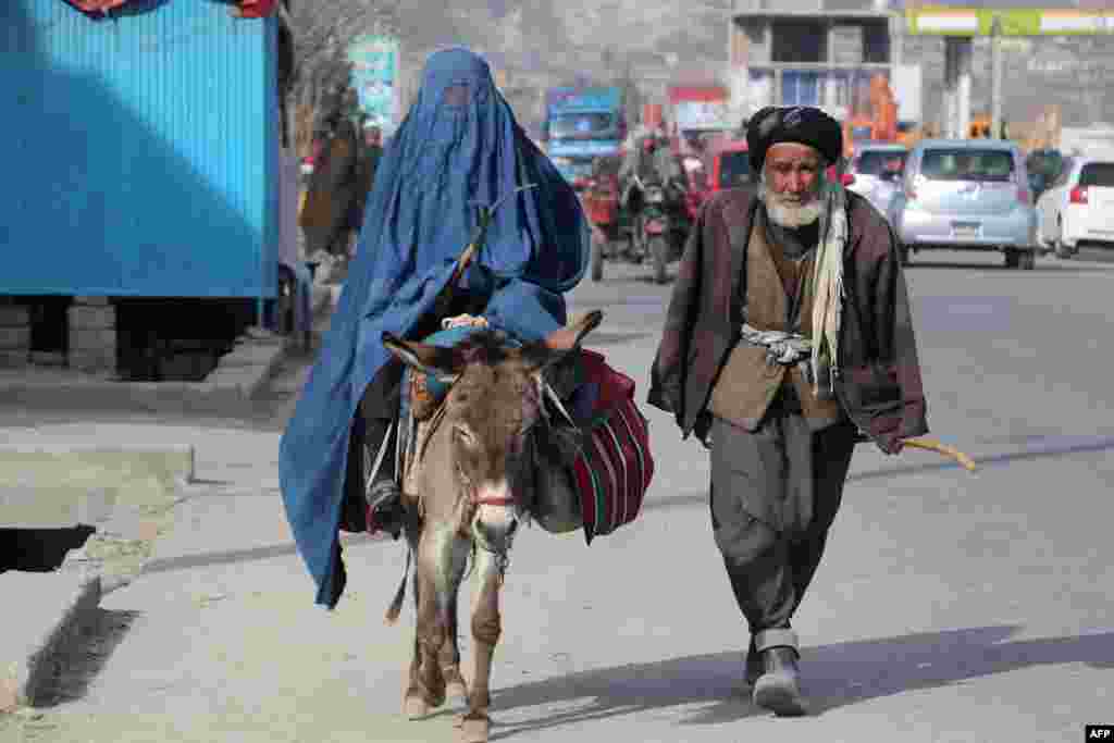Seorang pria berjalan di samping perempuan berburka yang mengendarai keledai di sepanjang jalan di Fayzabad, Afghanistan.