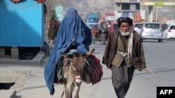 A man walks next a woman who is wearing a burqa and riding a donkey in Fayzaba, Afghanistan.