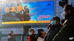 FILE - Residents wait to cross a street near a screen promoting the Chinese People's Liberation Army Air Force, in Beijing, Jan. 9, 2023. The Chinese military began combat strike drills the day before, the Chinese and Taiwanese defense ministries said.