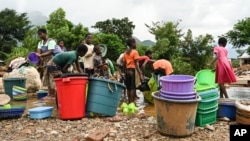 Women and children wash plastic kitchen utensils in a stream in Phalombe, southern Malawi, March 17, 2023. The area was hard hit by Cyclone Freddy. 