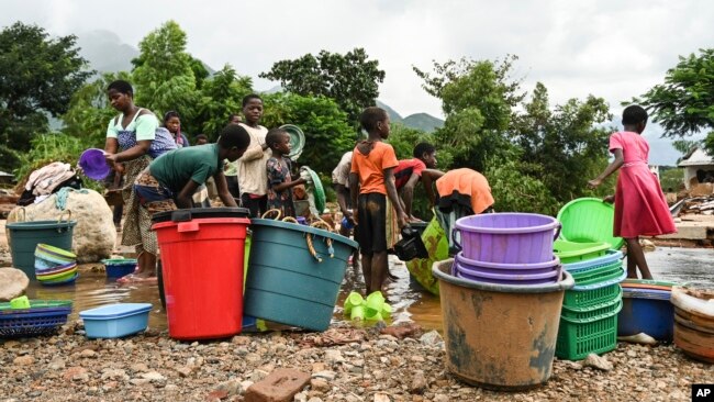Women and children wash plastic kitchen utensils in a stream in Phalombe, southern Malawi, March 17, 2023. The area was hard hit by Cyclone Freddy.