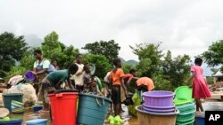 Women and children wash plastic kitchen utensils in a stream in Phalombe, southern Malawi, March 17, 2023.