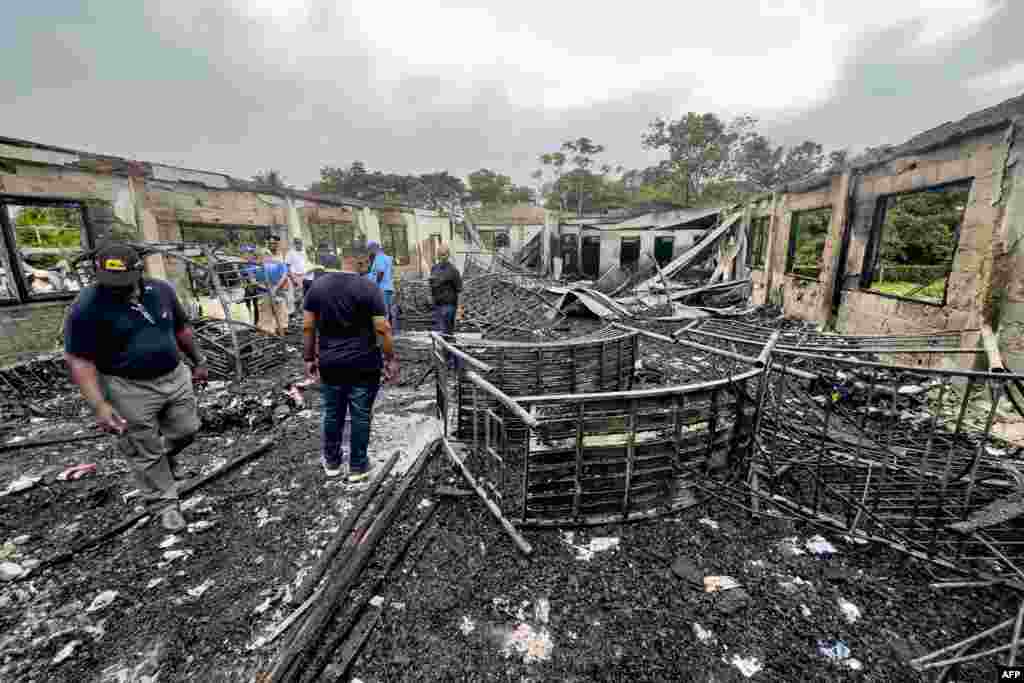 Investigators and government employees inspect the school dormitory where a fire killed at least 19 people in Mahdia, Guyana.