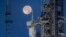 Bulan purnama terlihat di belakang Artemis I Space Launch System (SLS) dan pesawat ruang angkasa Orion di Kennedy Space Center NASA di Florida pada 14 Juni 2022. (Cory Huston/NASA via AP)
