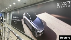 FILE - A woman walks near an advertisement billboard of a new electric vehicle from Chinese automaker Dongfeng at a train station in Beijing, April 20, 2024.