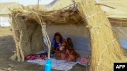 FILE - A picture taken on March 20, 2024, shows a displaced woman and her children sitting in the shade of a straw hut at a camp in southern Gadaref state for people who fled Khartoum and Jazira states in war-torn Sudan.