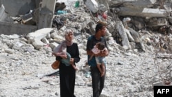 Warga Palestina tampak menggendong anak mereka saat berjalan di tengah reruntuhan di Khan Younis, di selatan Jalur Gaza, pada 4 Juli 2024. (Foto: AFP/Bashar Taleb)