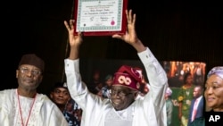 President-elect Bola Tinubu, center, displays his certificate, accompanied by his wife Oluremi Tinubu, right, and chairman of the Independent National Electoral Commission Mahmood Yakubu at a ceremony in Abuja, Nigeria, March 1, 2023.