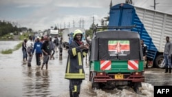 A Kenyan firefighter gives directions to commuters as residents inspect a road heavily affected by floods following torrential rains in Kitengela, May 1, 2024.