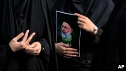 FILE - An Iranian woman holds a poster of the late President Ebrahim Raisi during a mourning ceremony for him at Vali-e-Asr square in downtown Tehran, Iran on May 20, 2024. 