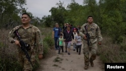 Beberapa migran China, yang berbaur dengan migran Amerika Tengah, dikawal oleh anggota Garda Nasional Angkatan Darat Texas setelah kelompok itu diselundupkan menyeberangi sungai Rio Grande dari Meksiko di Fronton, Texas (foto: dok). 