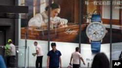 People walk past a billboard for Swiss luxury watch retailer Blancpain at an upscale shopping mall in Beijing, on June 13, 2023. (AP Photo/Mark Schiefelbein)