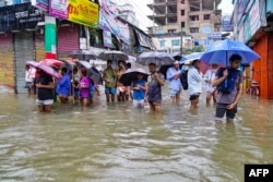 Orang-orang membawa payung, berjalan di jalanan yang tergenang banjir di Feni, 22 Agustus 2024. (AFP)