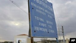 FILE - A woman walks by a sign at the U.N.-controlled buffer zone near Larnaca, Cyprus, on Jan. 8, 2009. Three U.N. soldiers had to be treated for minor injuries after Turkish Cypriots attacked peacekeepers who obstructed crews working on a road that would encroach on the zone.