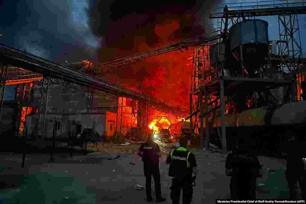 Ukrainian law enforcement officers stand next to the burning industrial facility following a missile strike in the village of Hoholeve, Poltava region.