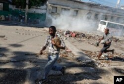 FILE—Men run for cover as riot police launch tear gas in an effort to disperse people near the National Palace, in Port-au-Prince, Haiti, Tuesday, April 2, 2024.