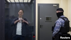 Wall Street Journal reporter Evan Gershkovich, who is in custody on espionage charges, makes a heart-shaped gesture inside an enclosure for defendants before a court hearing in Moscow, April 23, 2024.