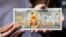 FILE - A protester shows a fake banknote depicting a duck during a pro-democracy rally demanding Thailand's king hands back royal assets to the people, reforms on monarchy, Bangkok, Nov. 25, 2020. 