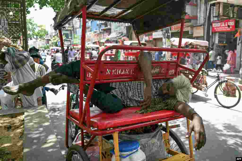 A man sleeps on his rickshaw along a street on a hot summer day in New Delhi.