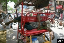 Seorang pria tertidur di atas rickshaw (sejenis becak) miliknya di pinggir sebuah jalan pada hari musim panas yang terik di New Delhi, India.
