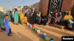 FILE - Residents wait to collect food in containers from a soup kitchen in Omdurman, Sudan, March 11, 2024. Nearly five million people in the country are close to famine as Sudan's civil war passes the one-year mark.