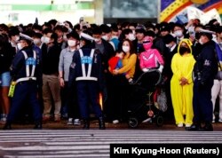 Warga yang mengenakan kostum berdiri di samping polisi yang mengendalikan massa yang berkumpul untuk merayakan Halloween di Shibuya di Tokyo, Jepang, 31 Oktober 2022. (Foto: REUTERS/Kim Kyung-Hoon)