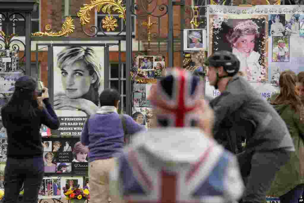 People stand in front of pictures of Princess Diana at the gates of Kensington Palace in London.