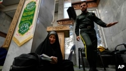 A woman fills out her ballot as a policeman walks past during the parliamentary and Assembly of Experts elections at a polling station in Tehran, Iran, March 1, 2024. 