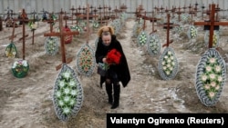 Một phụ nữ địa phương đặt hoa lên nấm mộ của những người vô danh bị lính Nga sát hại ở Ukraine.