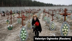 Місцева мешканка покладає квіти на могили невідомих людей, вбитих російськими військовими в Україні