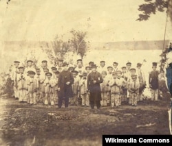 This 1865 photograph shows French missionary Eugene Casimir Chirouse, left, and an unidentified priest standing with students at the Tulalip Mission School, Tulalip, Washington.