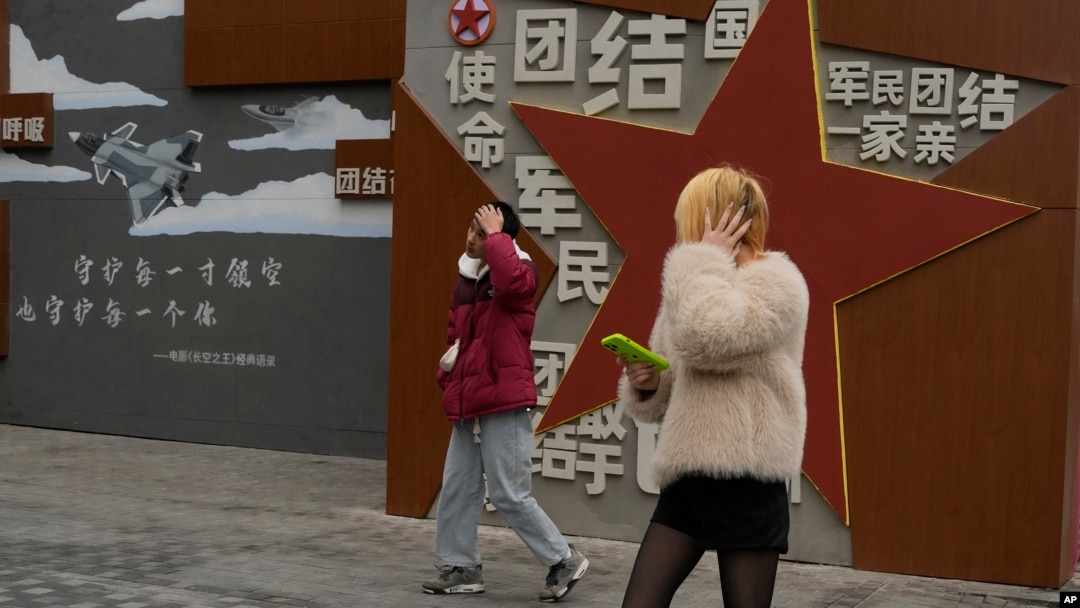 两个年轻人走过北京街头一堵政府的宣传墙。（2024年1月17日）