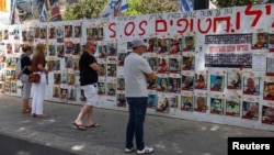 Personas se detienen delante de una pared con carteles en apoyo de los rehenes que fueron secuestrados durante el mortal ataque del 7 de octubre contra Israel por parte del grupo islamista palestino Hamás, en Tel Aviv, Israel, el 23 de abril de 2024.